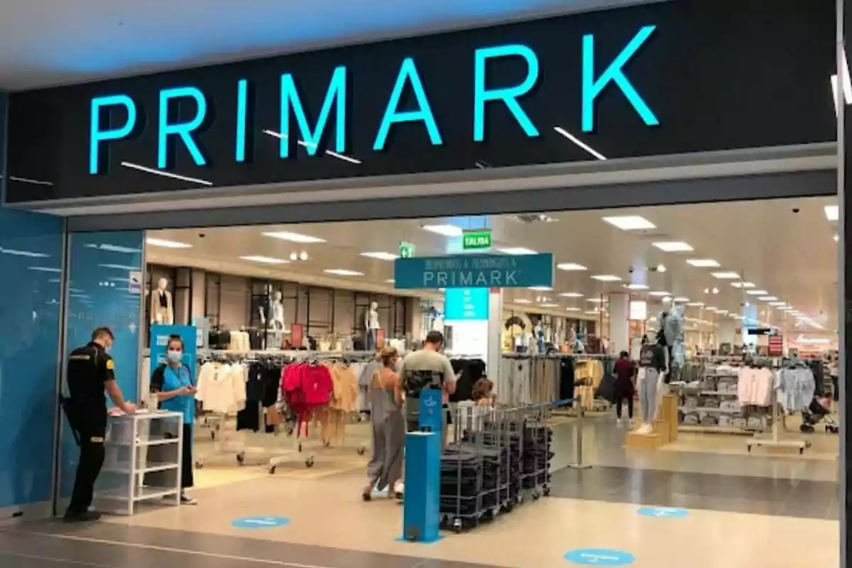 Entrada de una tienda Primark con personas entrando y saliendo, y un guardia de seguridad en la entrada.