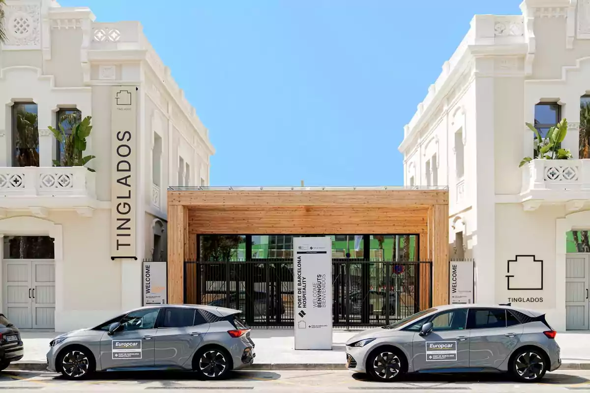 Dos coches grises estacionados frente a un edificio blanco con detalles arquitectónicos ornamentados y un letrero que dice "TINGLADOS".