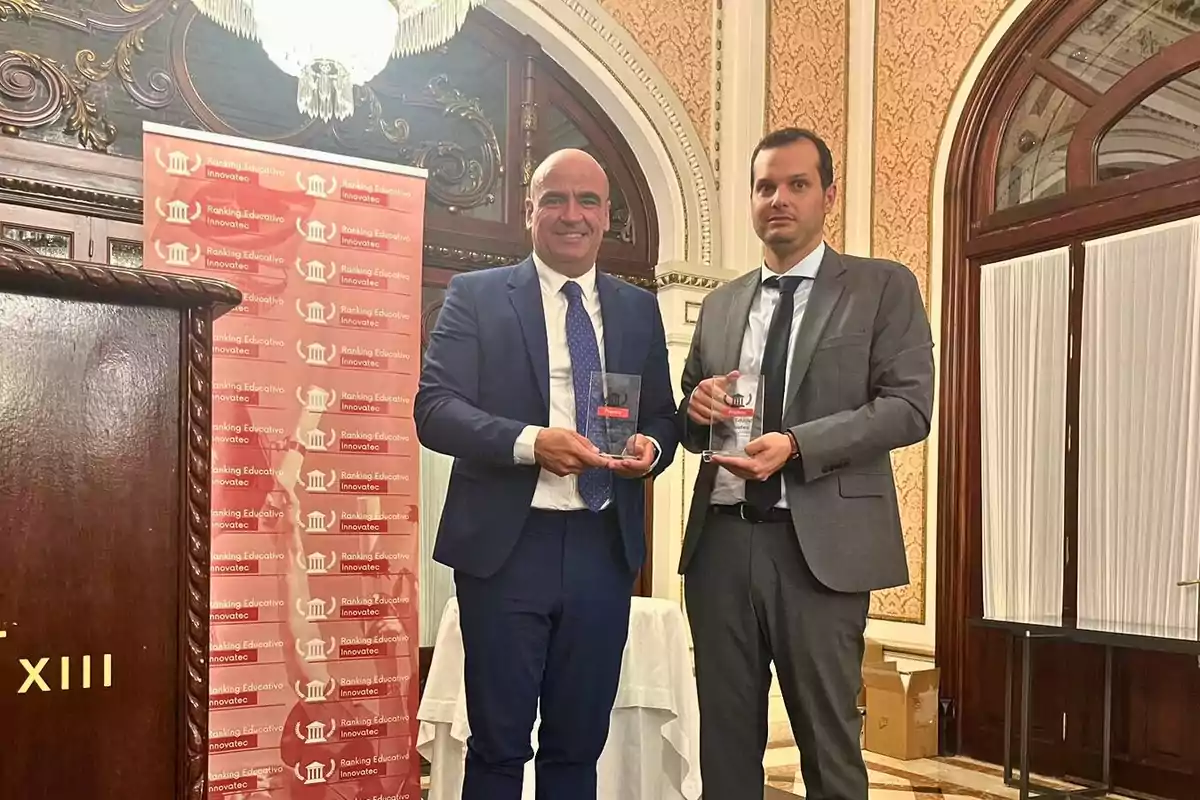 Dos hombres en trajes sosteniendo trofeos en una ceremonia de premiación con un fondo de pancarta roja que dice "Ranking Educativo Innovatec" en un salón elegante.