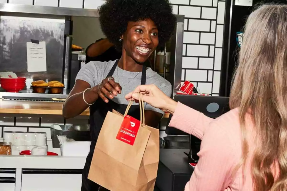 A smiling person hands a paper bag to a customer at a food counter. A smiling person hands a paper bag to a customer at a food counter.
