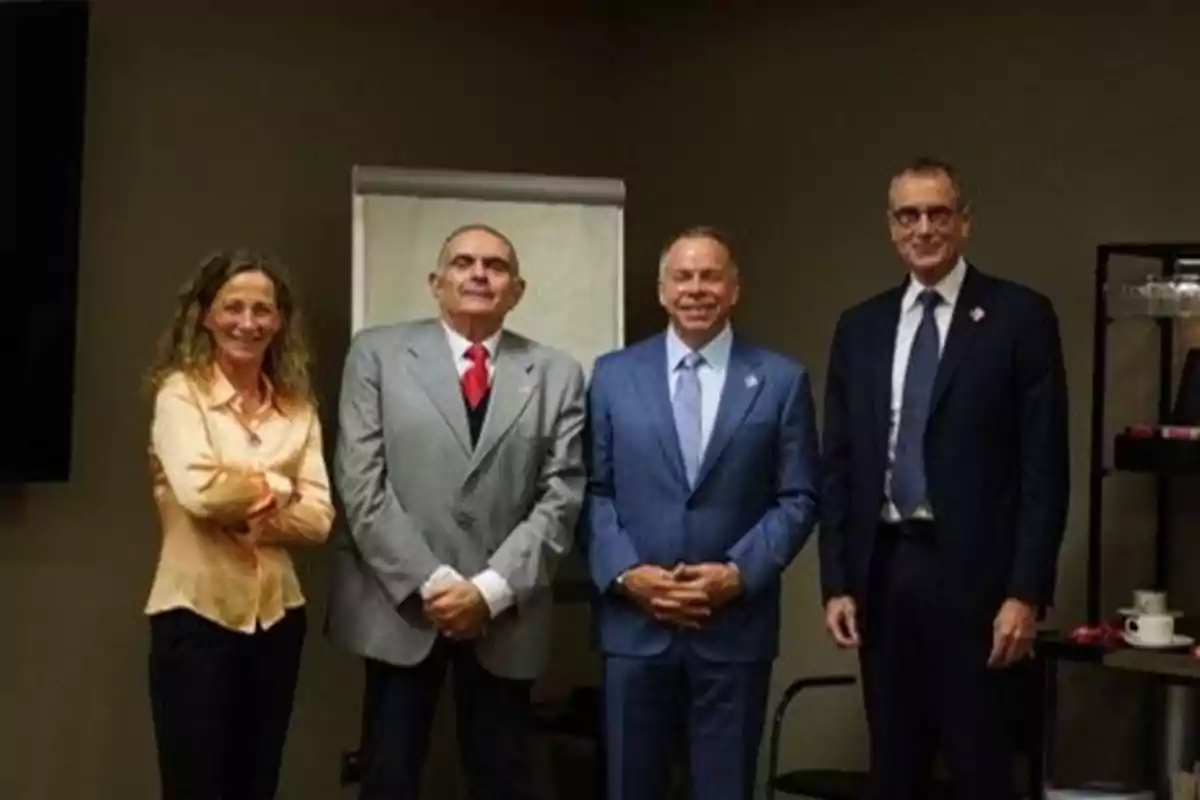 Cuatro personas posan juntas en una sala de conferencias, tres hombres y una mujer, todos vestidos formalmente.