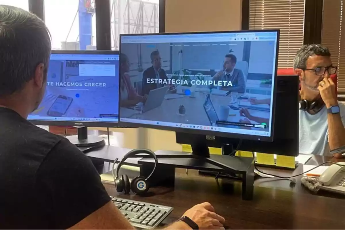 Dos personas trabajando en una oficina con dos monitores que muestran páginas web relacionadas con estrategias de crecimiento.