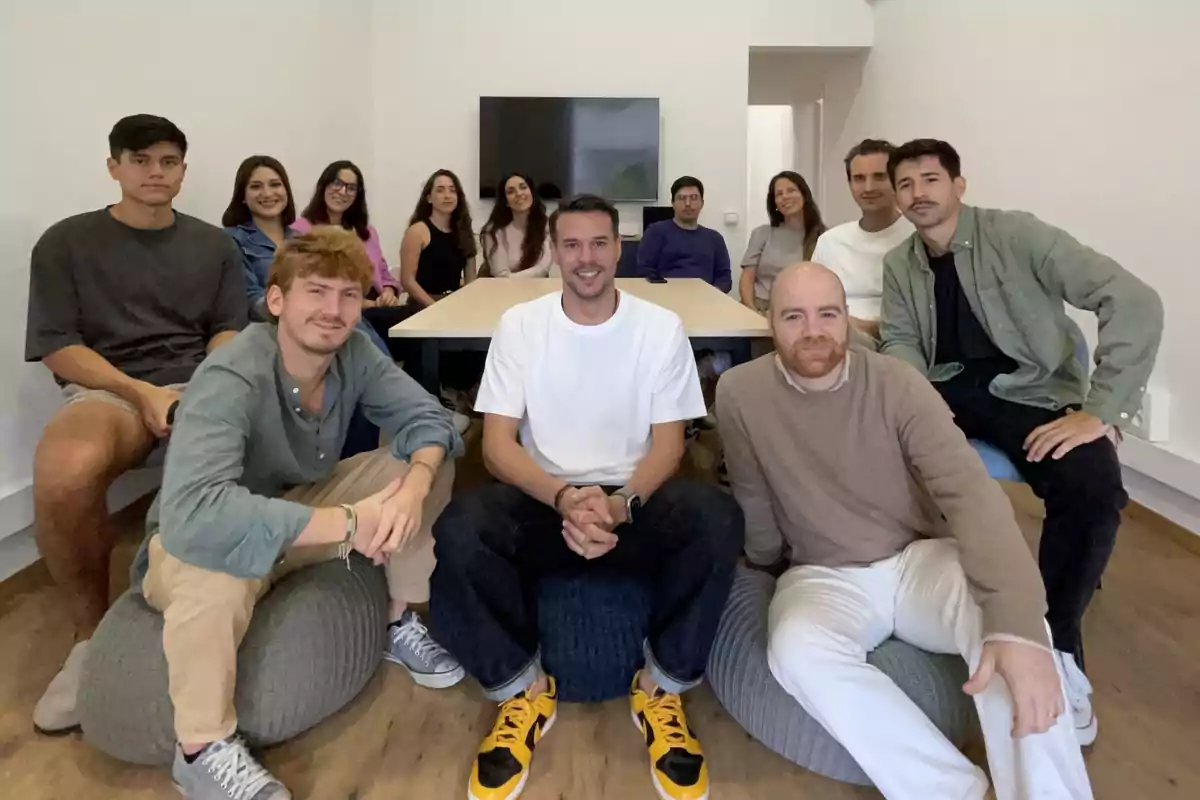 Un grupo de personas sentadas y de pie en una sala de reuniones, con una mesa y una pantalla al fondo.