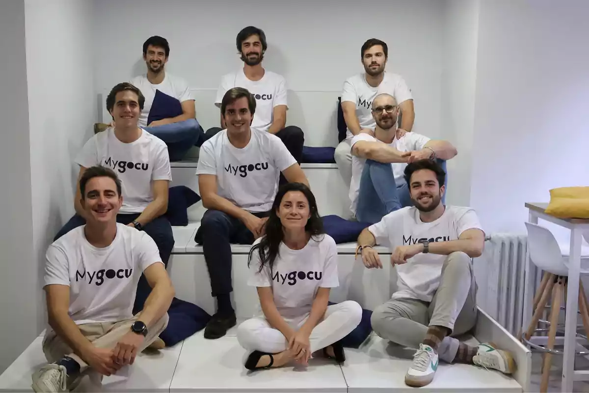 Un grupo de personas sentadas en una estructura escalonada, todas vistiendo camisetas blancas con el logo de "Mygocu".