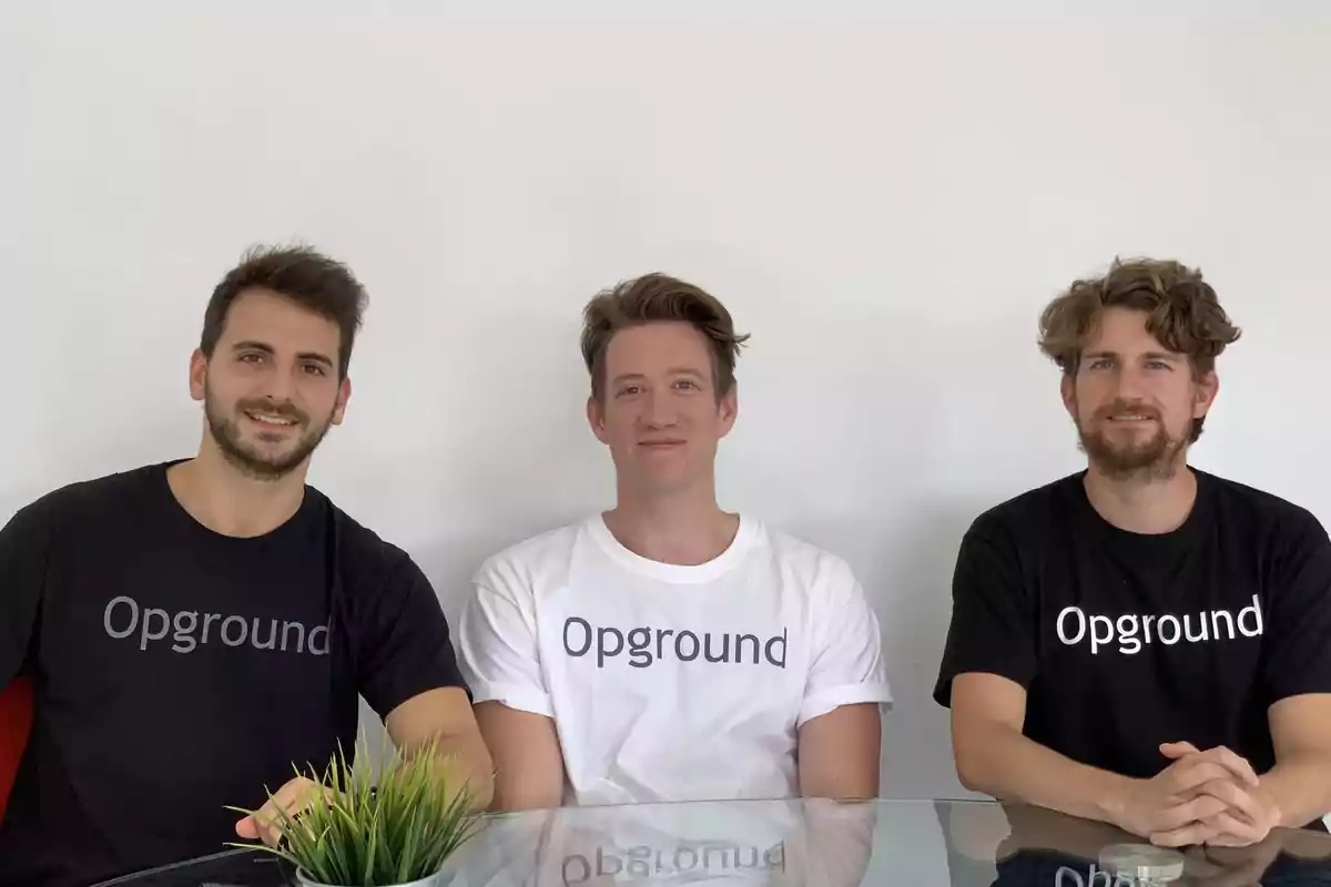 Tres hombres sentados en una mesa, todos vistiendo camisetas con el logo de "Opground".