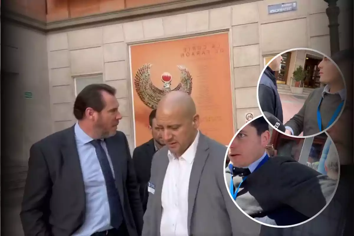 Un grupo de hombres con trajes formales camina por una calle frente a un edificio con un cartel grande en la pared.