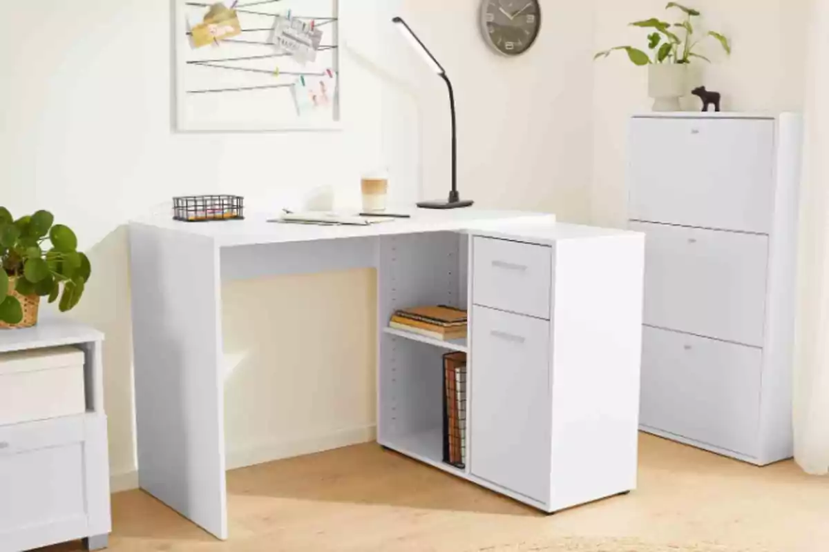 Una oficina en casa con un escritorio blanco en forma de L, una lámpara de escritorio negra, una planta en una maceta, un reloj de pared, un tablero de notas y un archivador blanco. Una oficina en casa con un escritorio blanco en forma de L, una lámpara de escritorio negra, una planta en una maceta, un reloj de pared, un tablero de notas y un archivador blanco.