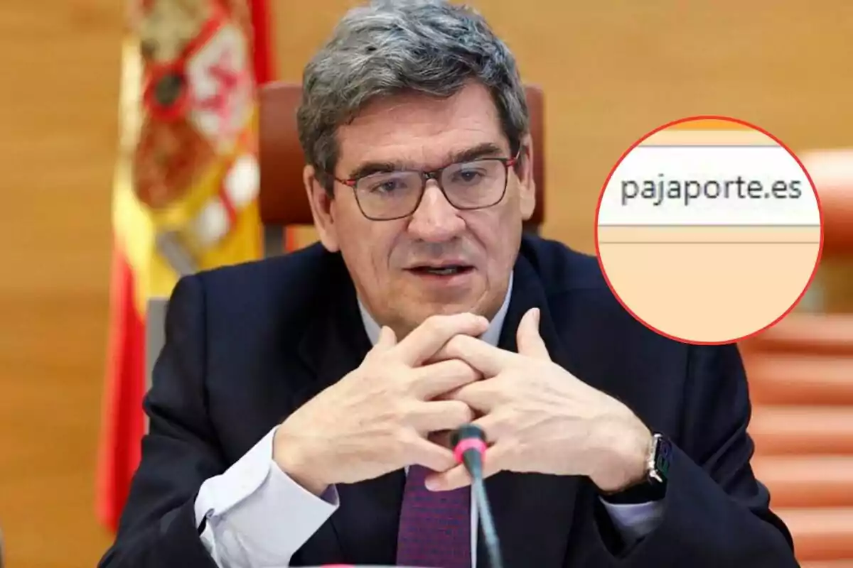 Hombre con gafas y traje oscuro hablando en un micrófono con una bandera de España de fondo y un círculo resaltando un error tipográfico en una dirección web.