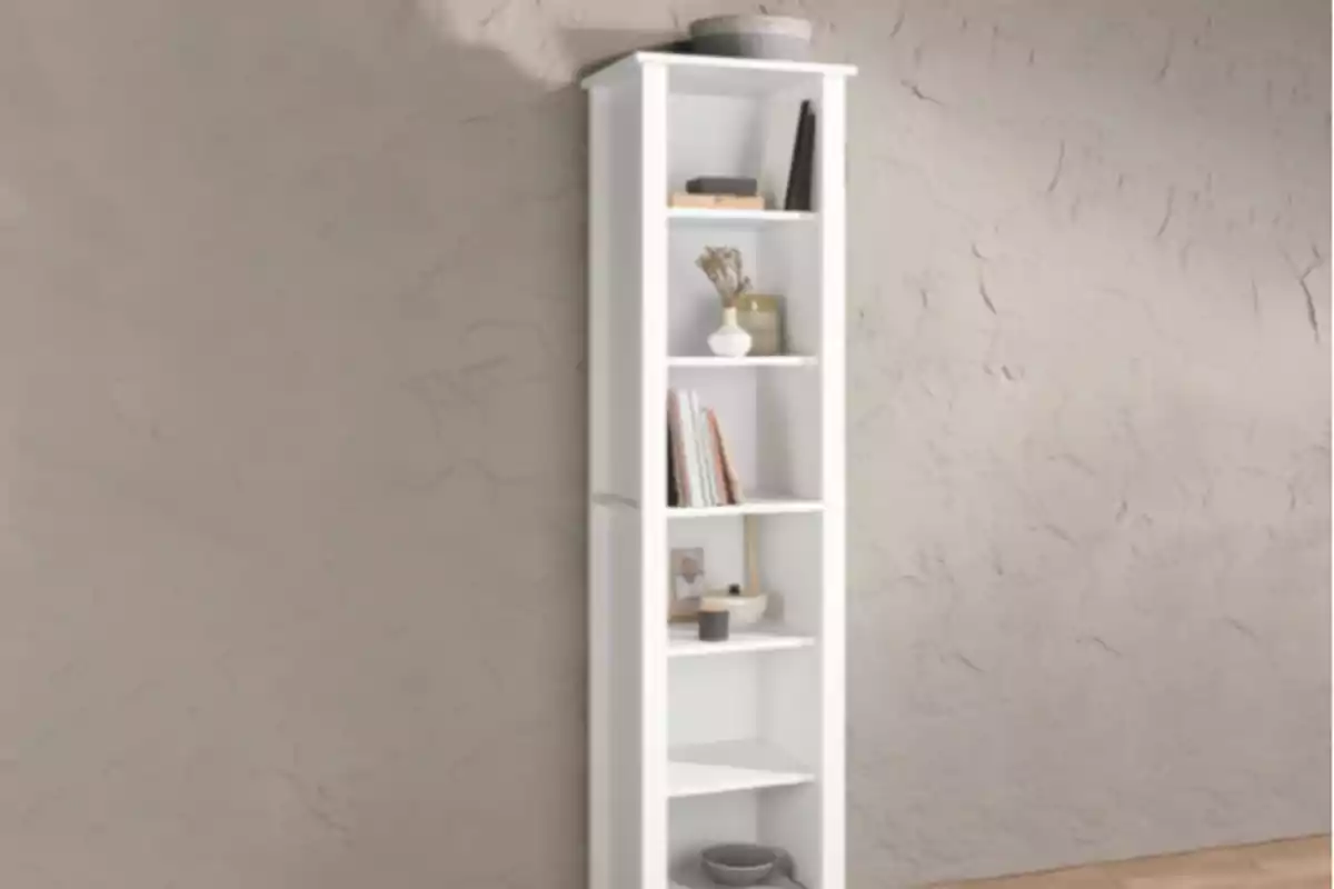 Librero blanco esquinero con varios estantes, decorado con libros, una planta y algunos objetos pequeños, colocado junto a una pared de textura rugosa. Librero blanco esquinero con varios estantes, decorado con libros, una planta y algunos objetos pequeños, colocado junto a una pared de textura rugosa.