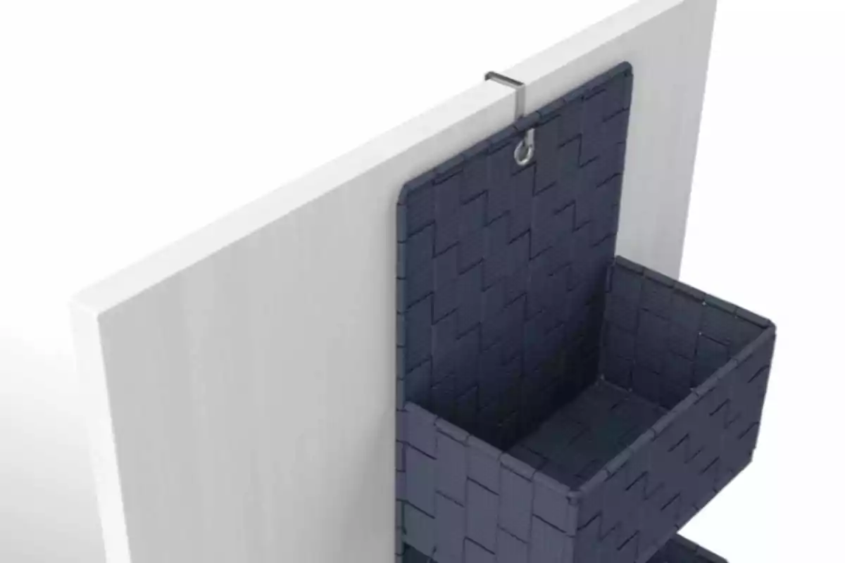 Cesta de almacenamiento colgante de color oscuro sujeta a un panel blanco. Cesta de almacenamiento colgante de color oscuro sujeta a un panel blanco.