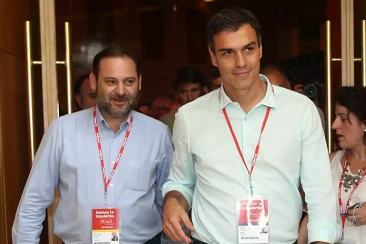 Dos hombres con camisas claras y credenciales colgadas al cuello caminan juntos en un evento.