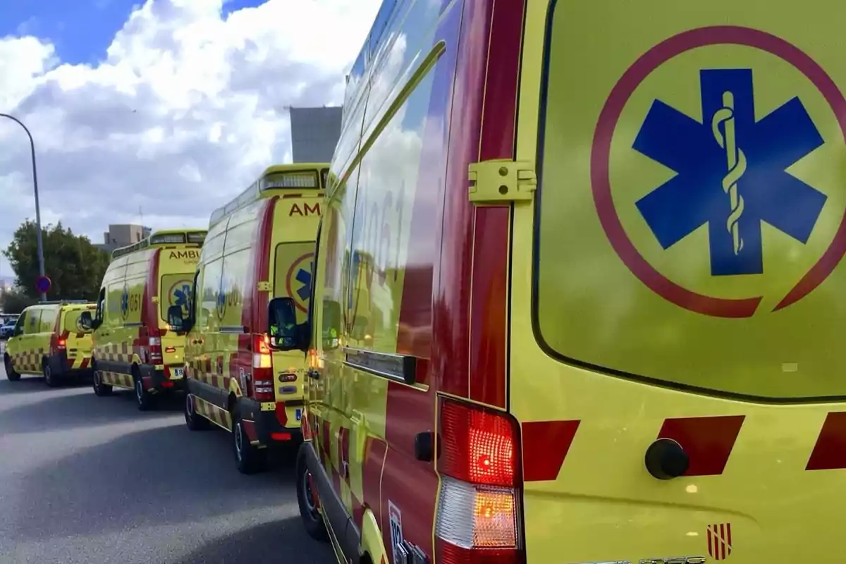 Una fila de ambulancias amarillas y rojas estacionadas en una calle bajo un cielo parcialmente nublado.