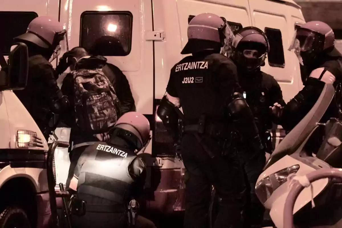 A group of police officers with helmets and vests is gathered around a person next to a white vehicle.