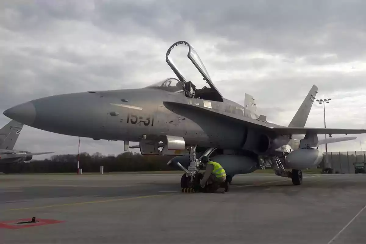 Un avión de combate en una pista con la cabina abierta y una persona trabajando en el tren de aterrizaje.