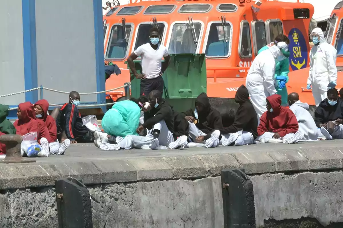 A group of people sitting on a dock next to an orange boat with medical personnel attending.