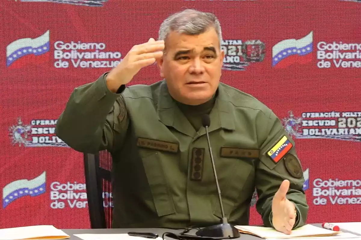 Un militar venezolano en uniforme verde oliva habla en una conferencia de prensa con un fondo rojo que tiene el logotipo del Gobierno Bolivariano de Venezuela.