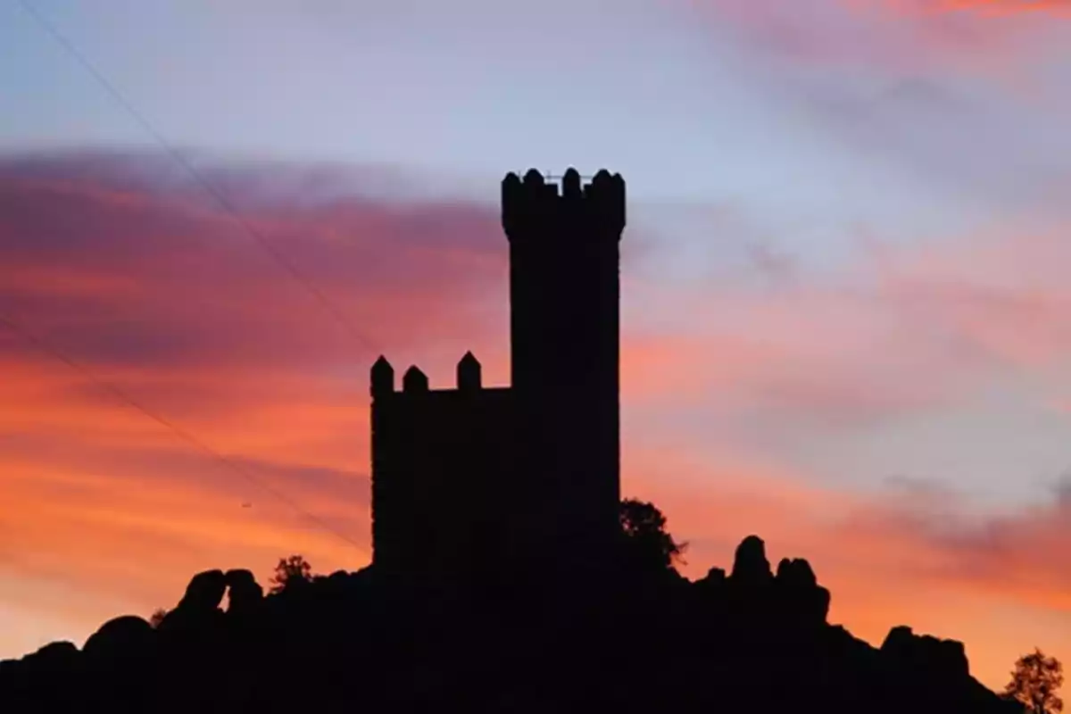 Silueta de una torre de castillo al atardecer con un cielo de colores cálidos.