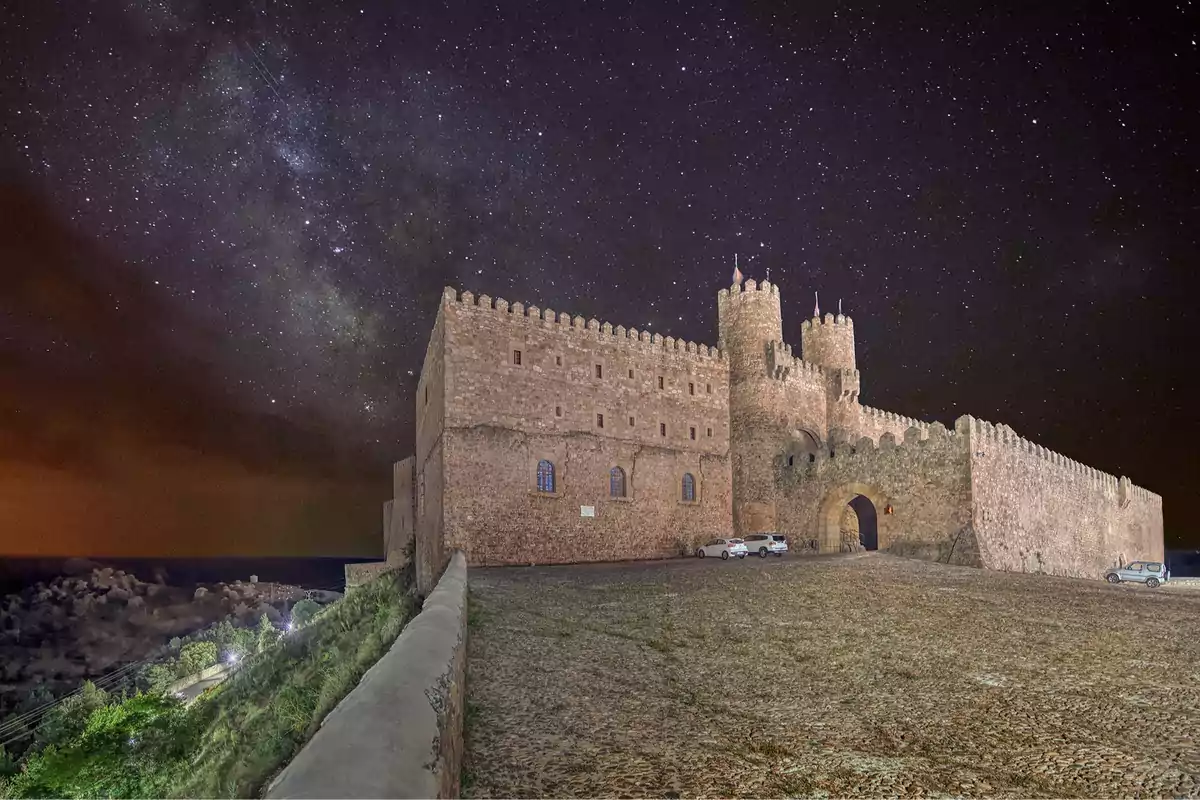 Un castillo medieval iluminado por la noche con un cielo estrellado de fondo. Un castillo medieval iluminado por la noche con un cielo estrellado de fondo.