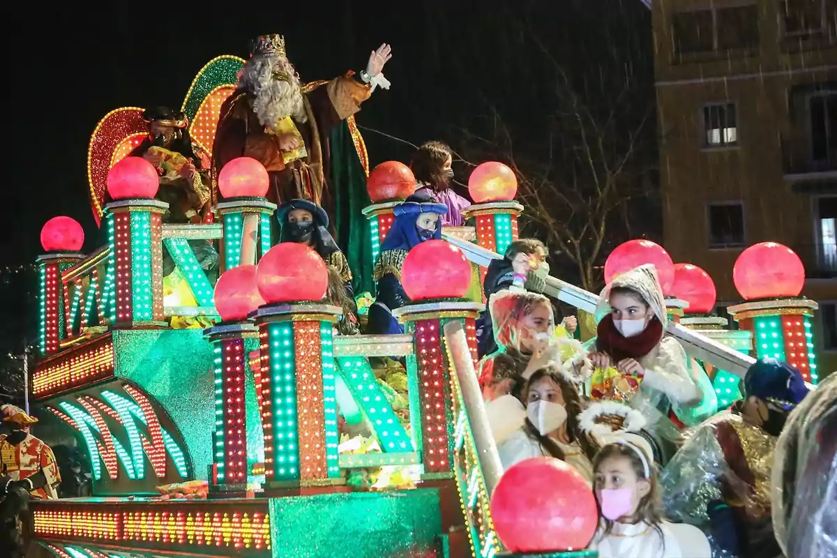 Un desfile nocturno con una carroza iluminada llena de personas disfrazadas y decoraciones coloridas.