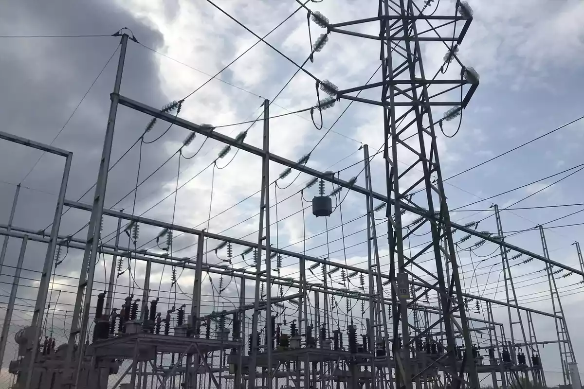Estructura metálica de una subestación eléctrica con cables y aisladores bajo un cielo nublado.