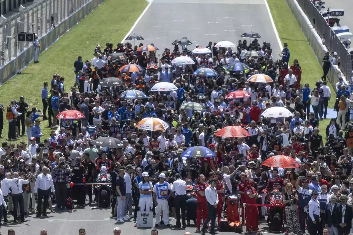 Una multitud de personas se reúne en una pista de carreras, muchas de ellas sosteniendo paraguas de diferentes colores.