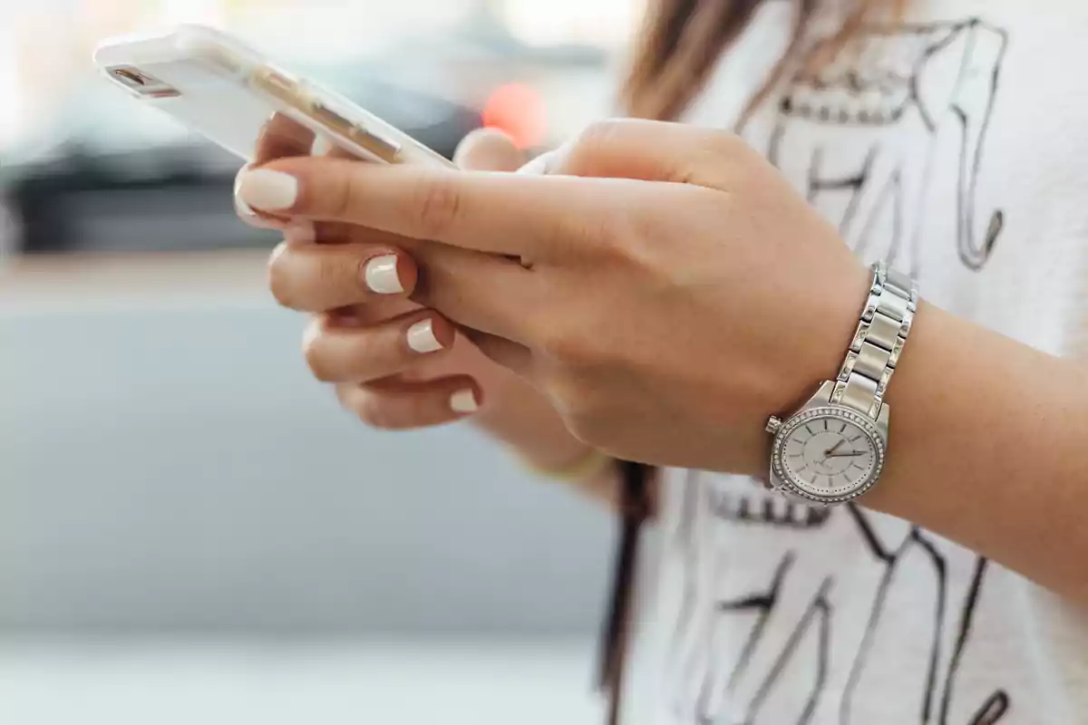 Persona usando un teléfono móvil con una mano y llevando un reloj de pulsera plateado. Persona usando un teléfono móvil con una mano y llevando un reloj de pulsera plateado.