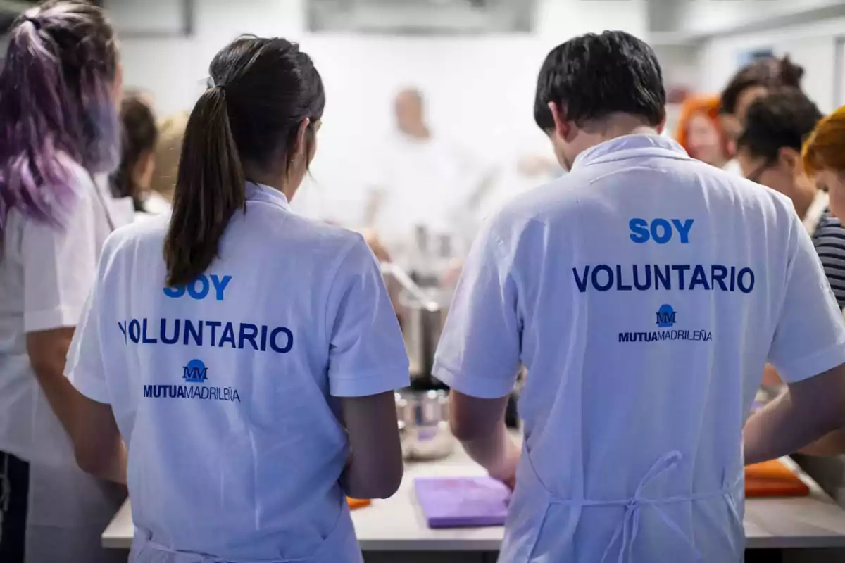 Personas con camisetas blancas que dicen "Soy voluntario" participan en una actividad grupal en un entorno de cocina.