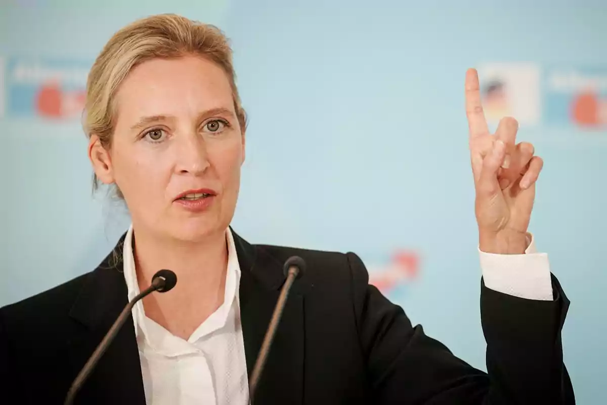 A person speaking at a conference with a microphone and raising a finger.