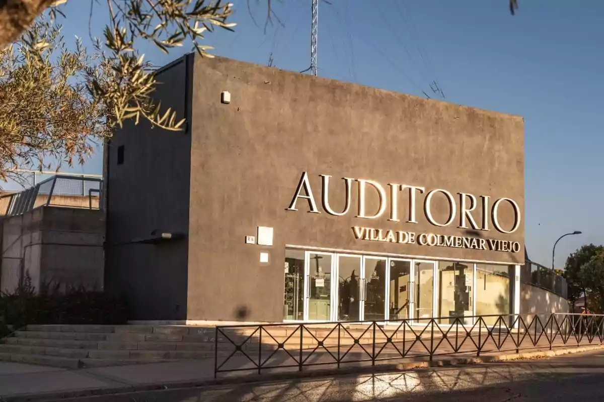 Edificio del Auditorio Villa de Colmenar Viejo con fachada de cemento y letras grandes iluminadas por el sol.