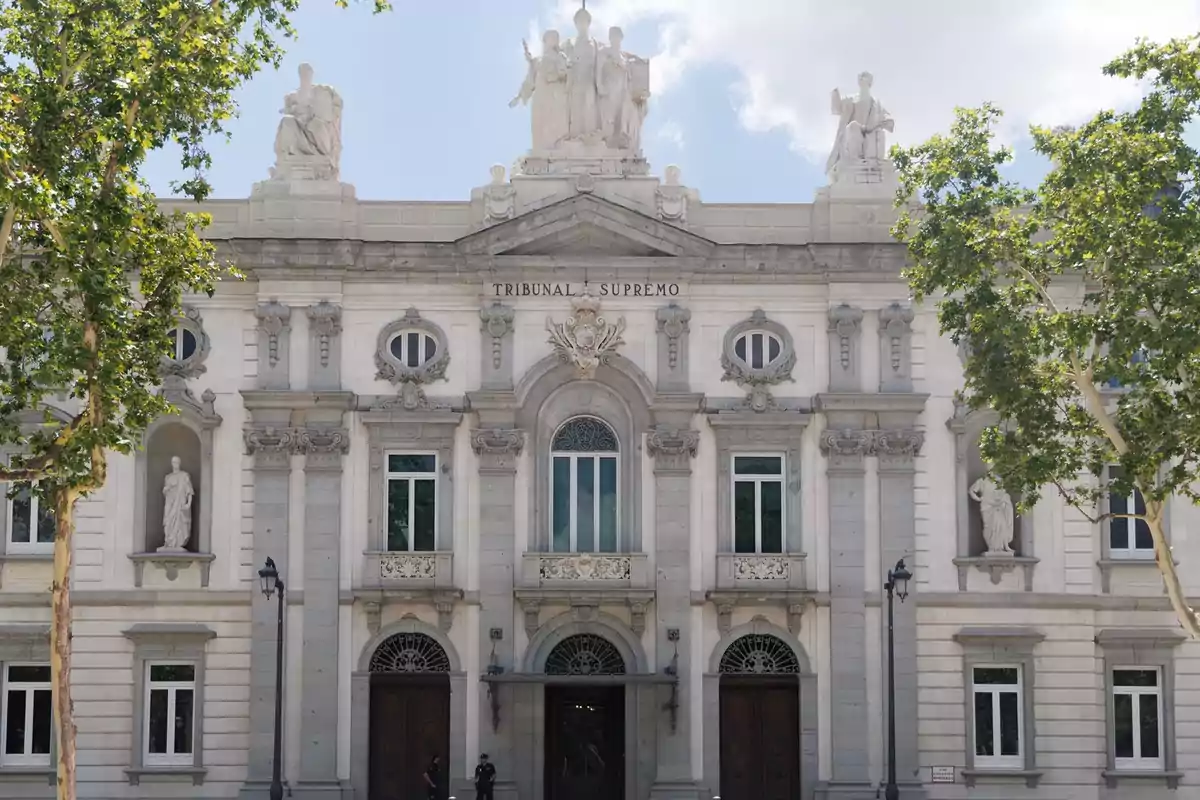 Fachada del Tribunal Supremo de España con esculturas y árboles en primer plano.