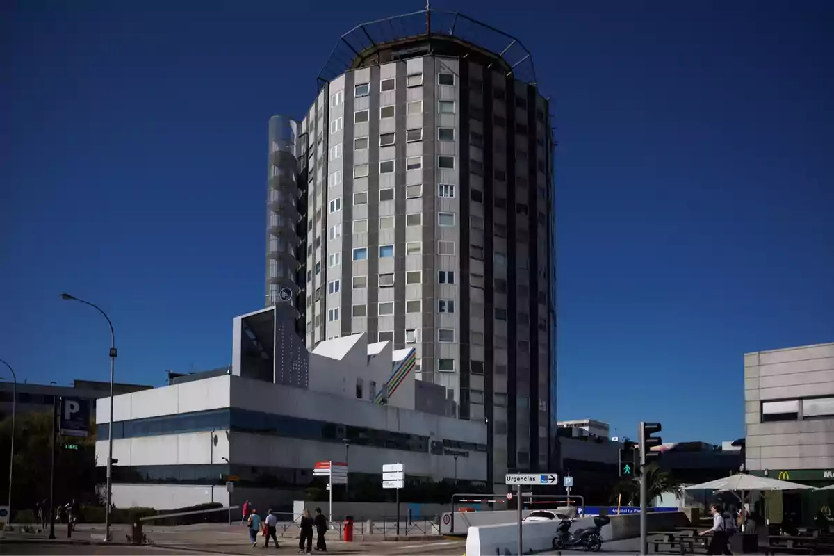 A tall, modern building with a cylindrical structure and square windows under a light blue sky.