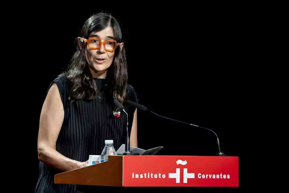 Una mujer con gafas naranjas habla en un podio del Instituto Cervantes.