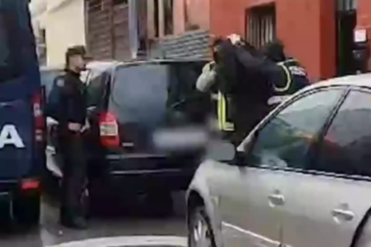 A scene on the street shows several police officers next to vehicles, one of them appears to be making an arrest.