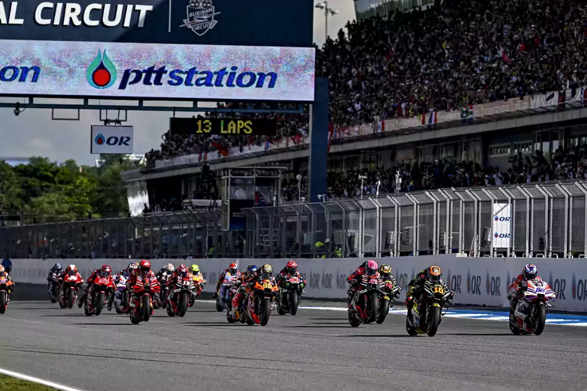 Motociclistas compitiendo en una carrera en el Circuito Internacional de Buriram, con una multitud de espectadores en las gradas y un letrero que indica 13 vueltas restantes.