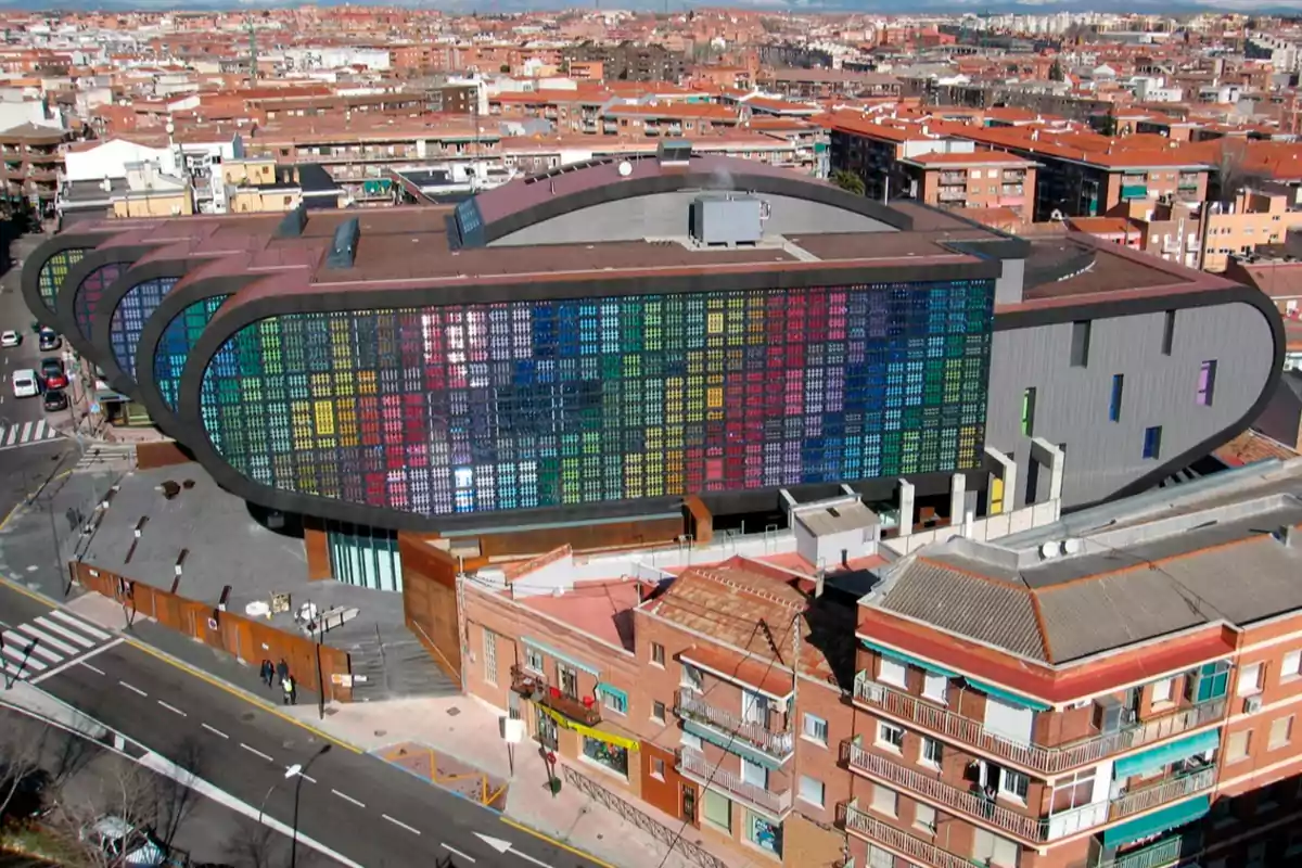 Vista aérea de un edificio moderno con una fachada de paneles de colores en un entorno urbano.