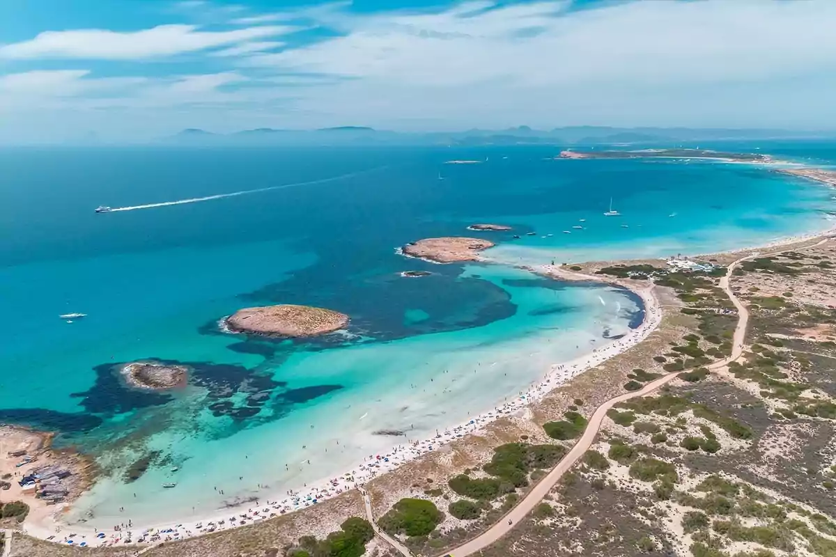 Vista aérea de una playa con aguas turquesas, arena blanca y pequeñas islas rocosas.