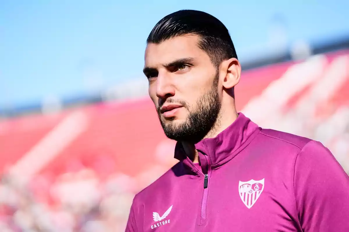 Un jugador de fútbol con una chaqueta morada del Sevilla FC en un estadio.