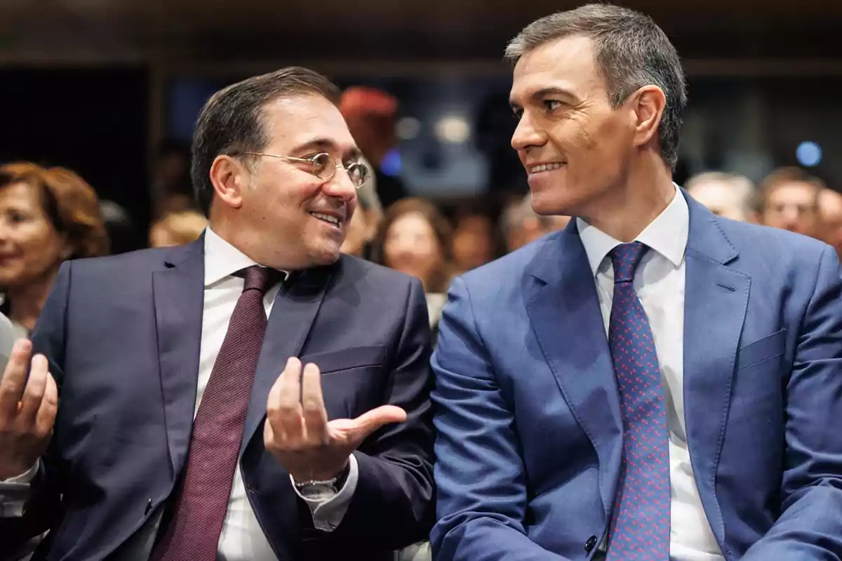 Dos hombres en trajes formales conversando y sonriendo en un evento.