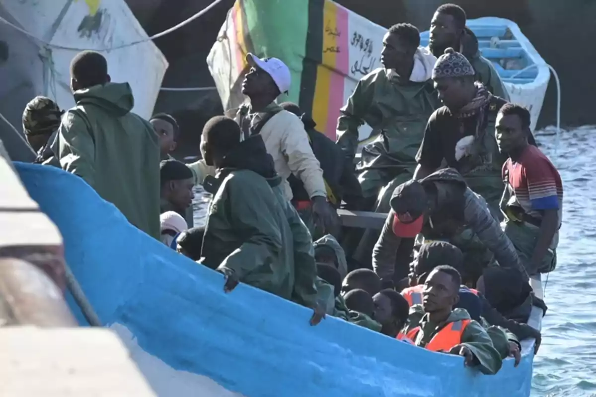 Un grupo de personas en un bote de pesca, algunas con chaquetas impermeables y otras con chalecos salvavidas, navegando en el agua cerca de otros botes.