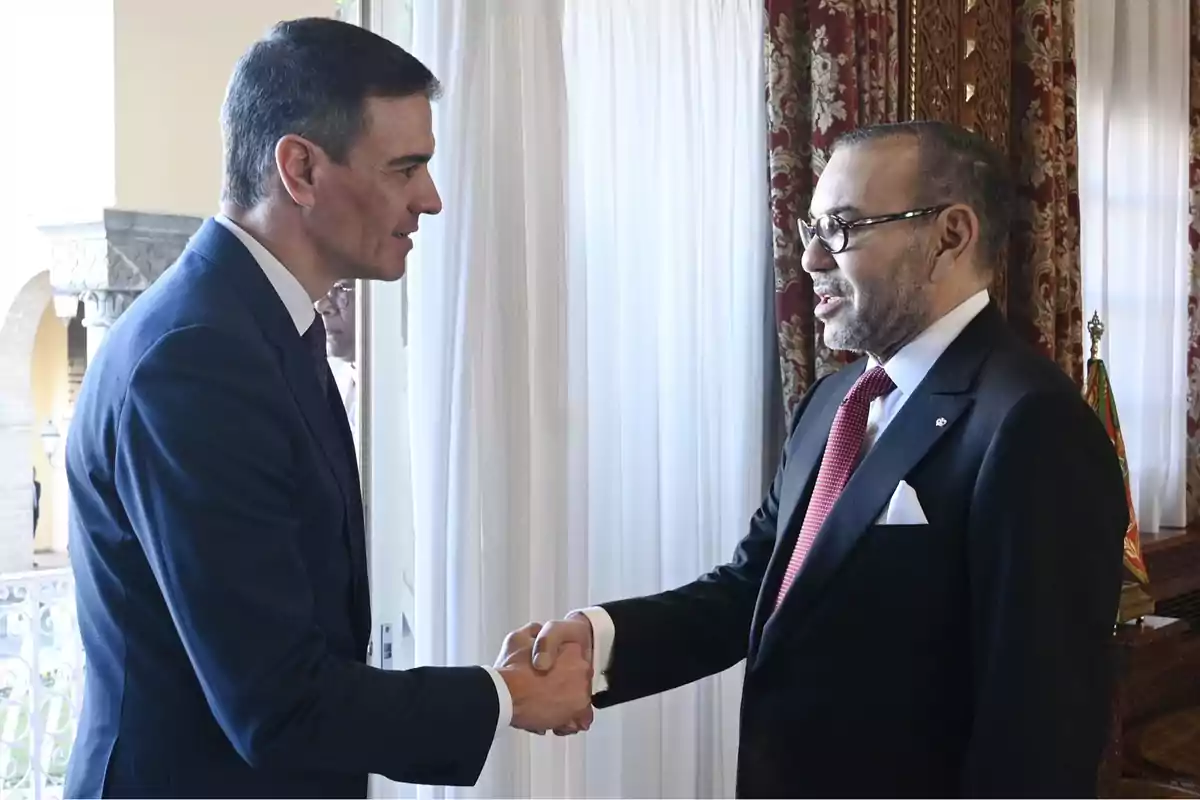 Dos hombres de traje estrechándose la mano en una sala con cortinas blancas y decoración elegante.