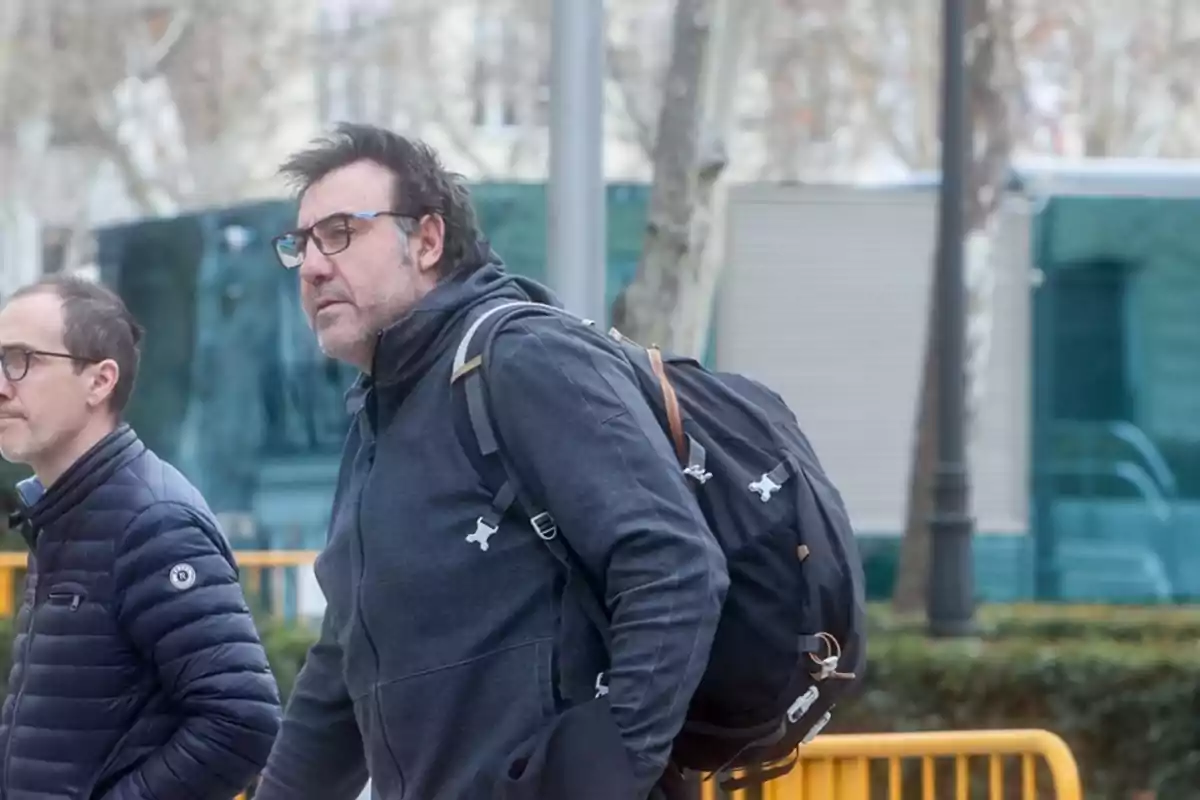 Dos hombres caminando al aire libre, uno de ellos lleva una mochila negra. Dos hombres caminando al aire libre, uno de ellos lleva una mochila negra.