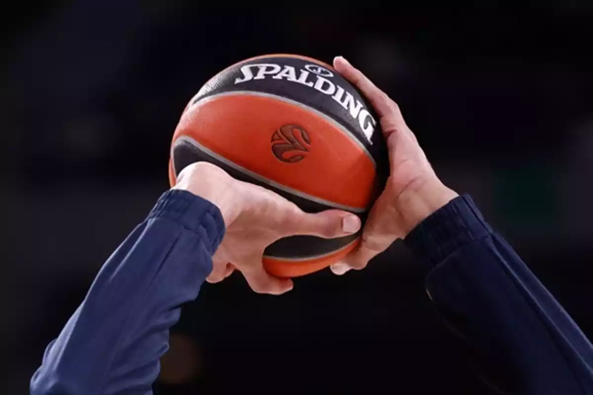 Manos sosteniendo un balón de baloncesto Spalding.