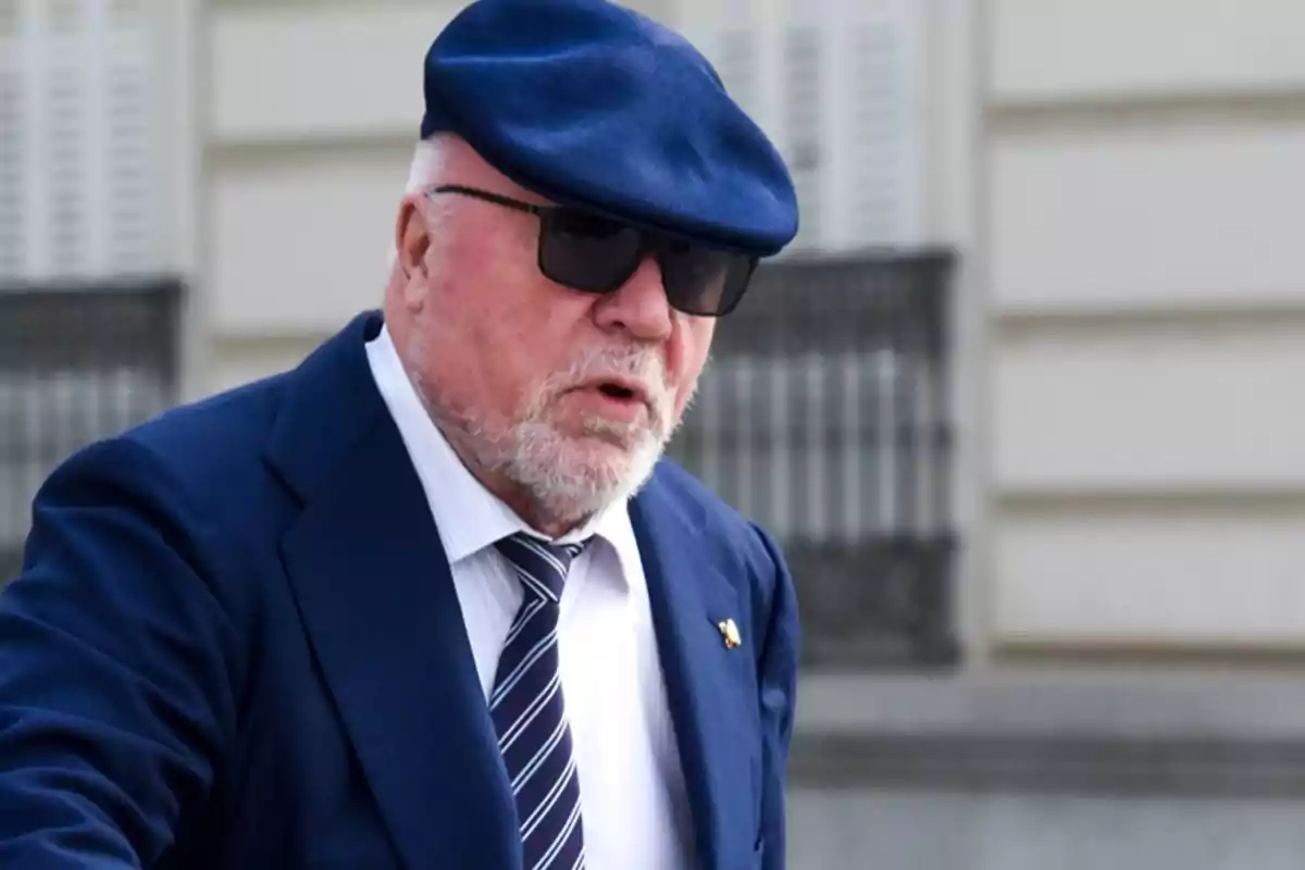 Un hombre con barba y gafas de sol lleva un traje azul y una boina del mismo color.