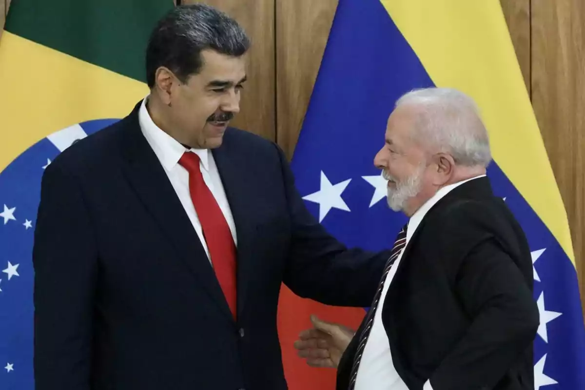 Dos hombres de traje y corbata se saludan frente a las banderas de Brasil y Venezuela.