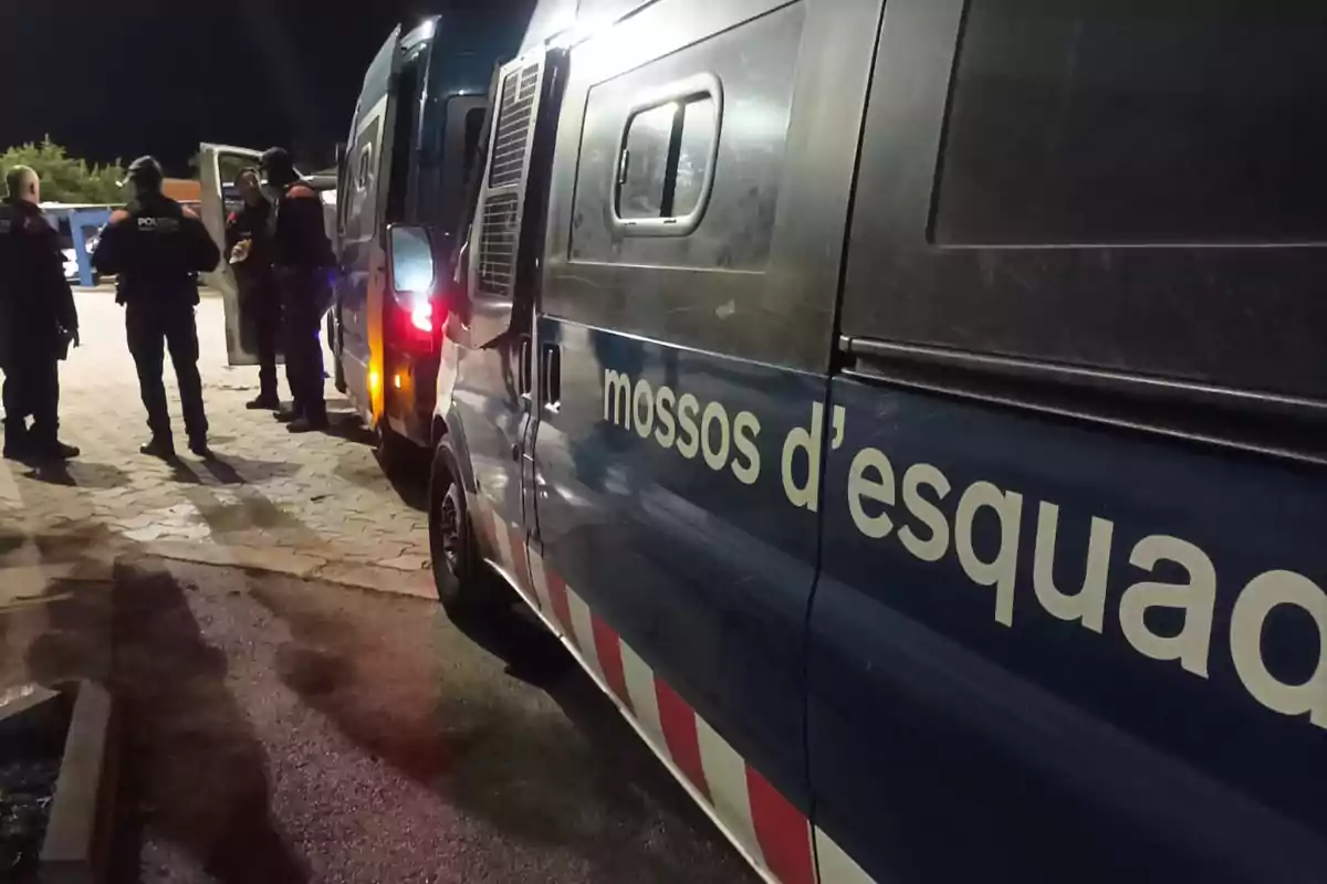 Furgoneta de los Mossos d'Esquadra estacionada junto a varios agentes de policía de pie conversando en una zona iluminada por la noche Furgoneta de los Mossos d'Esquadra estacionada junto a varios agentes de policía de pie conversando en una zona iluminada por la noche