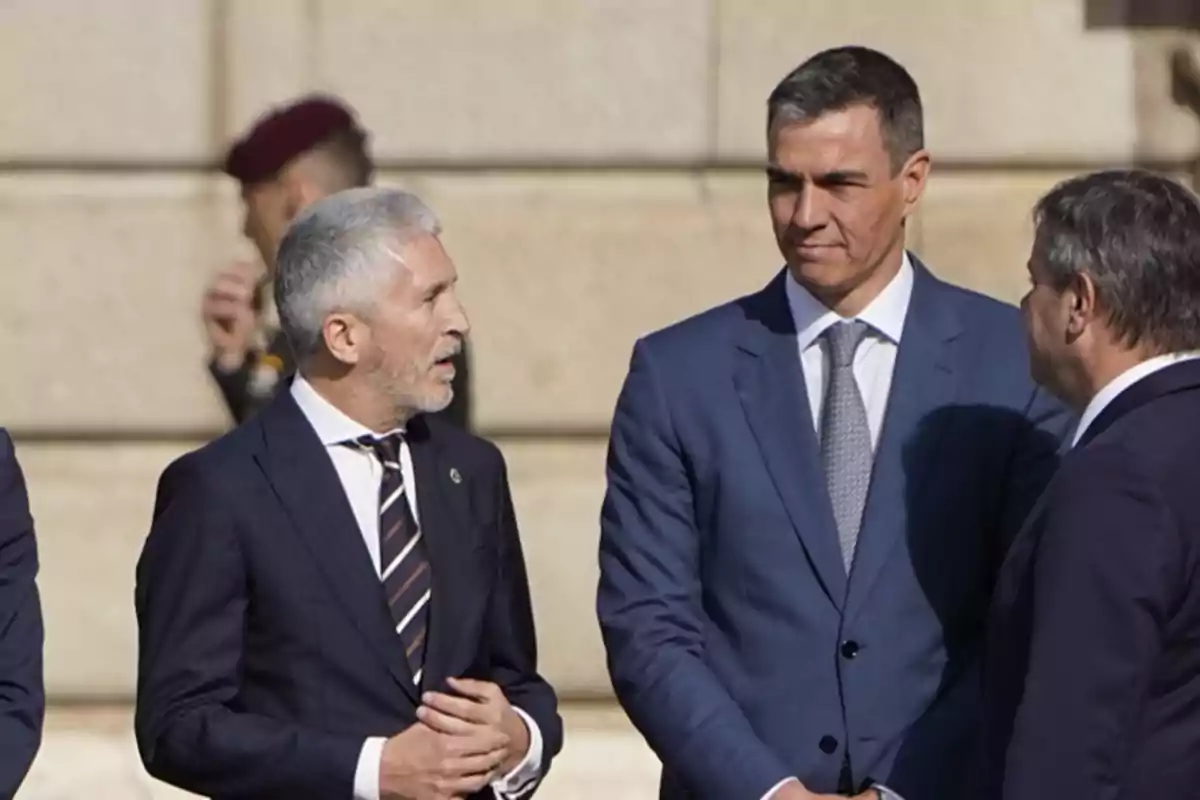 Tres hombres de traje conversan al aire libre frente a un edificio de piedra. Tres hombres de traje conversan al aire libre frente a un edificio de piedra.