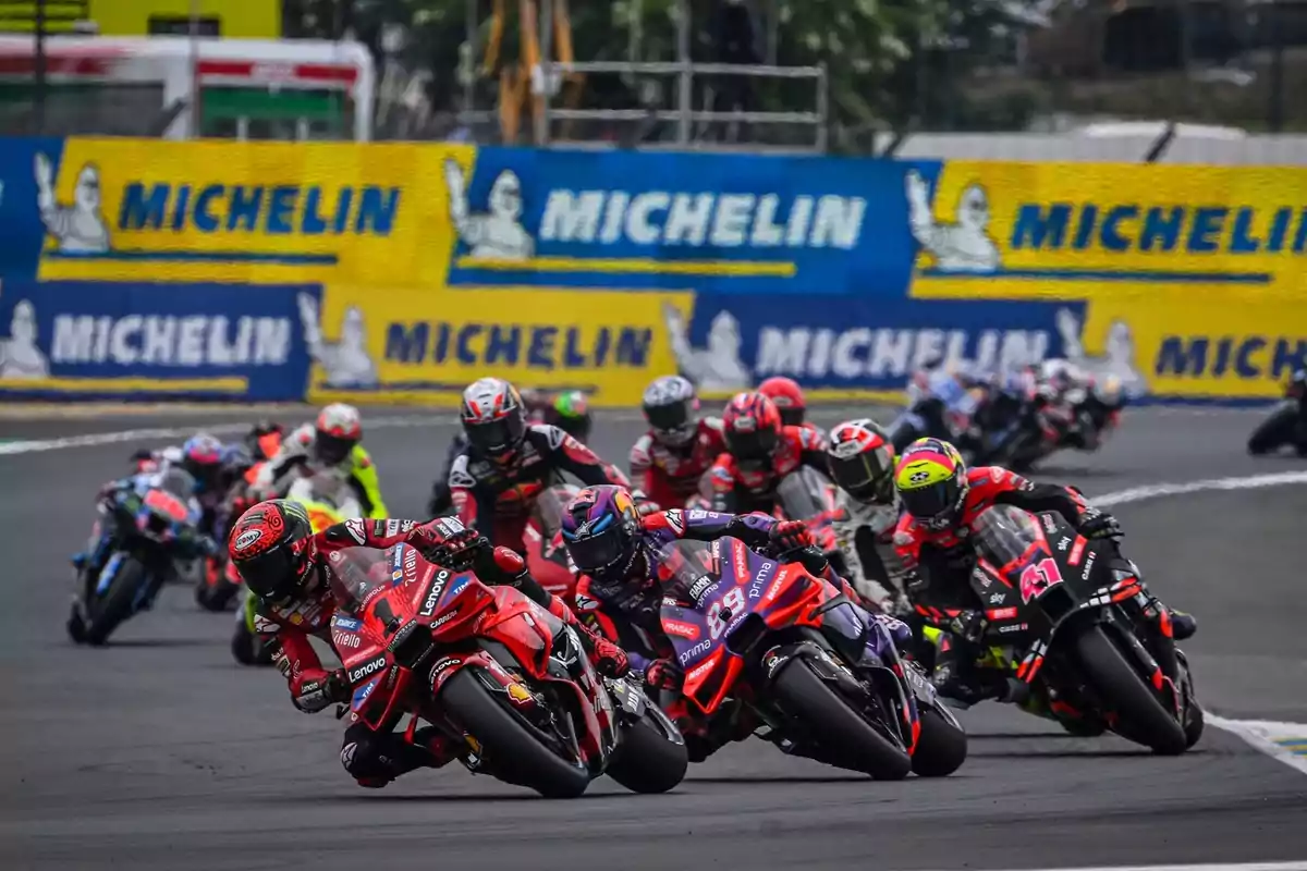 Competencia de motociclismo en una pista con varios pilotos en acción y publicidad de Michelin en el fondo.