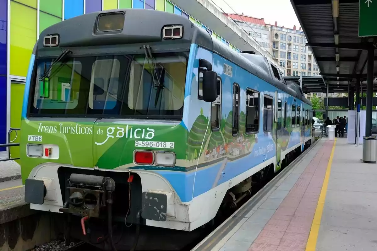 Un tren turístico de Galicia estacionado en una plataforma de una estación, con un diseño colorido en su exterior.