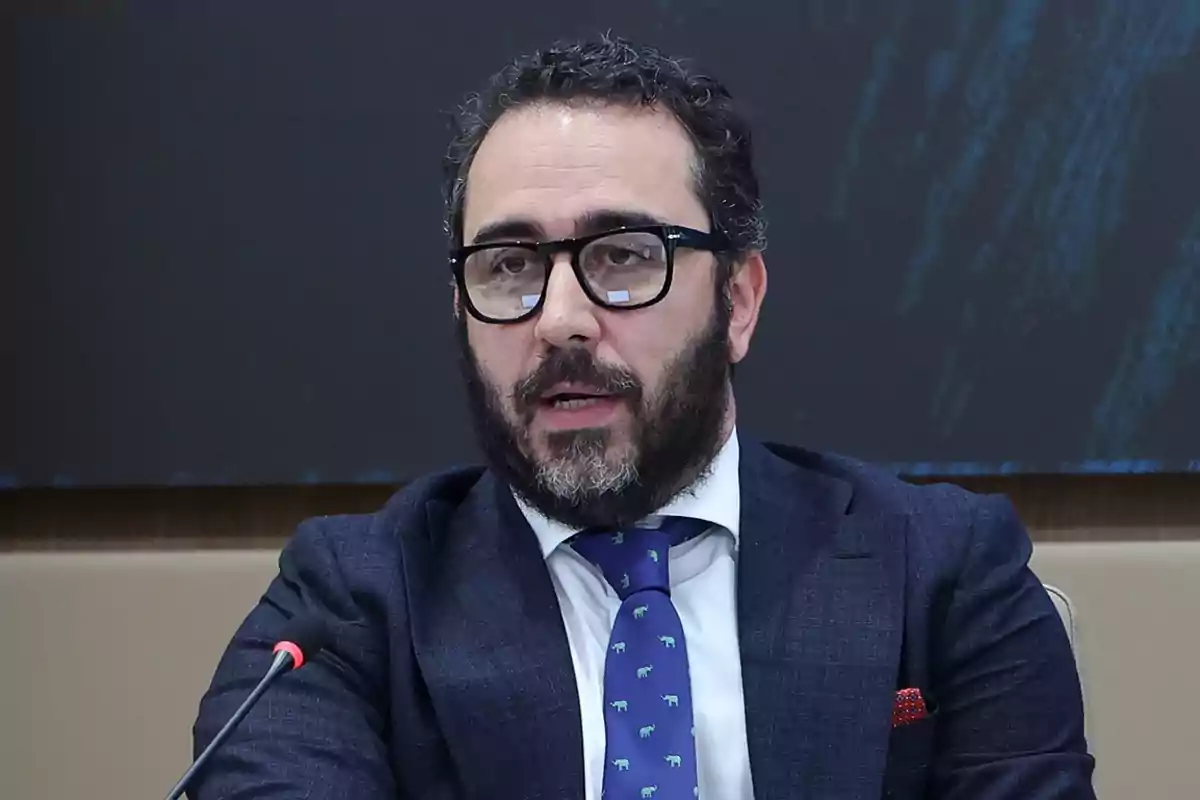 Un hombre con barba y gafas habla en un micrófono durante una conferencia.