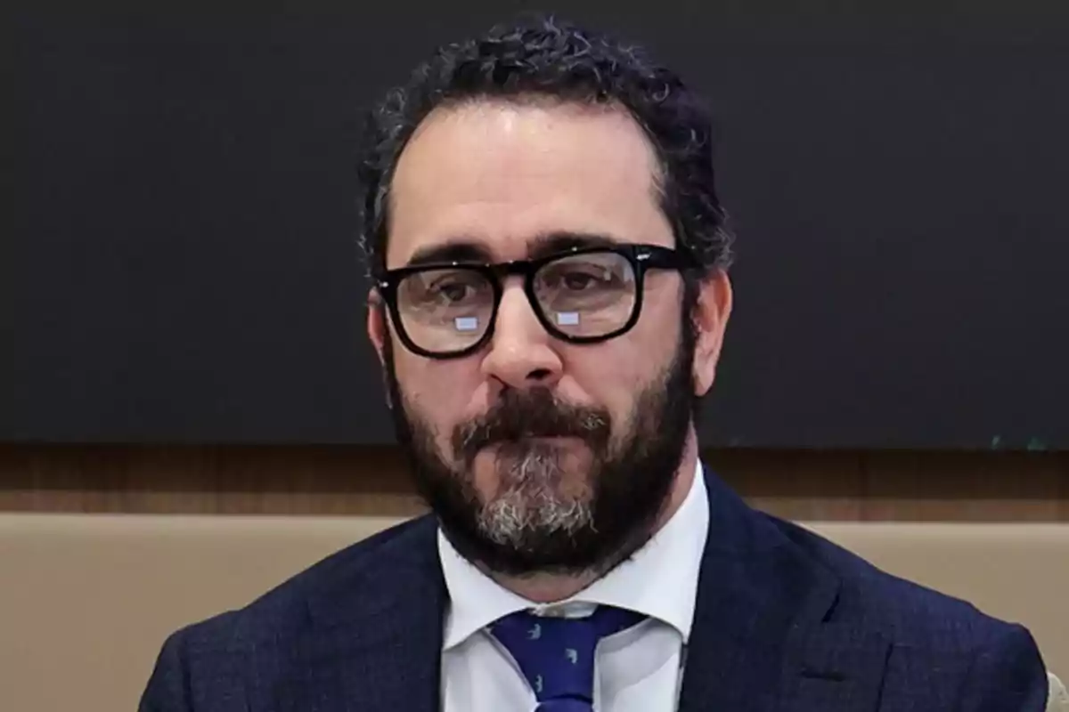 Hombre con barba y gafas vistiendo traje y corbata azul.